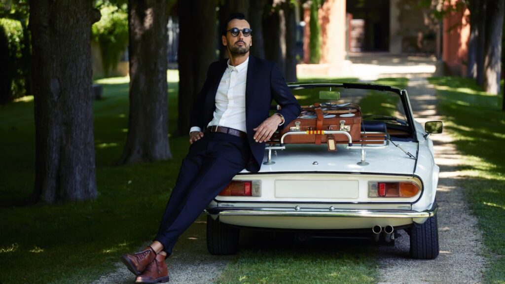 Man dressed in a suit and leaning on a nice car