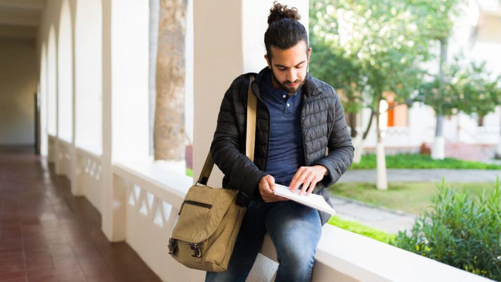 college man sitting on a ledge reading 