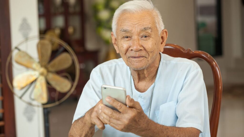 older man sitting at a table looking at his phone