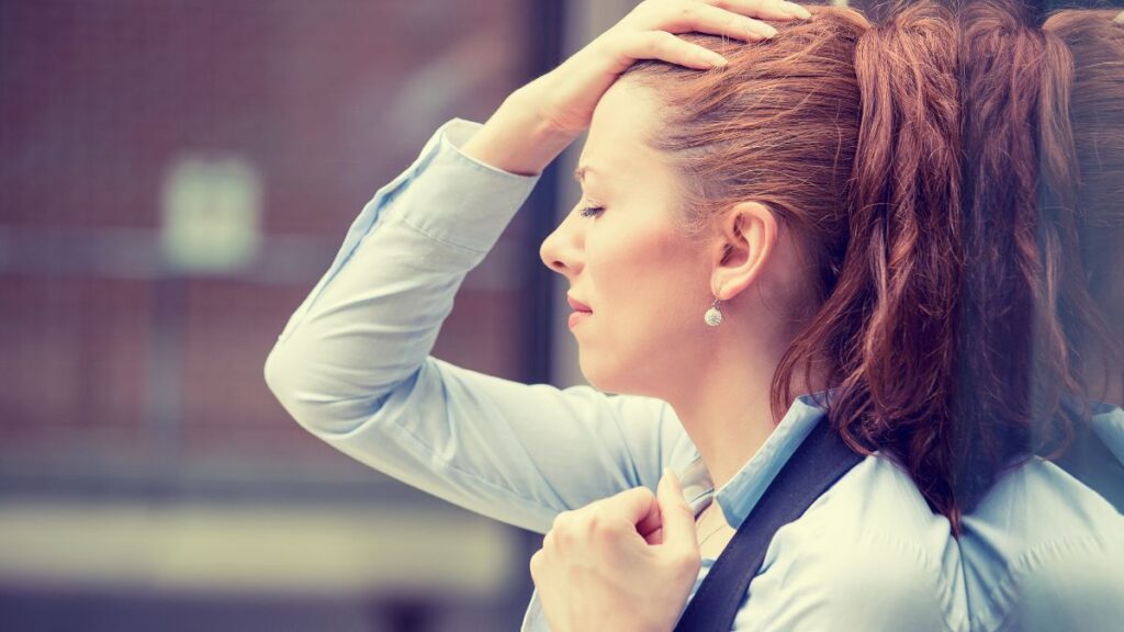 stressed out woman holding her head agains a window