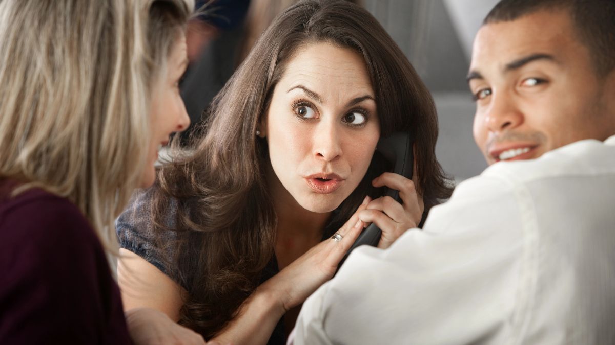 woman holding the phone looking annoyed at two people talking