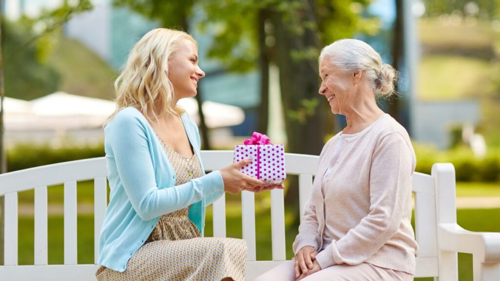 young woman giving older woman a gift on a bench