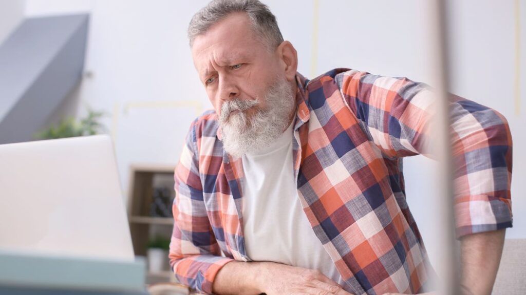 man with white beard, older looking uncomfortable on a desk