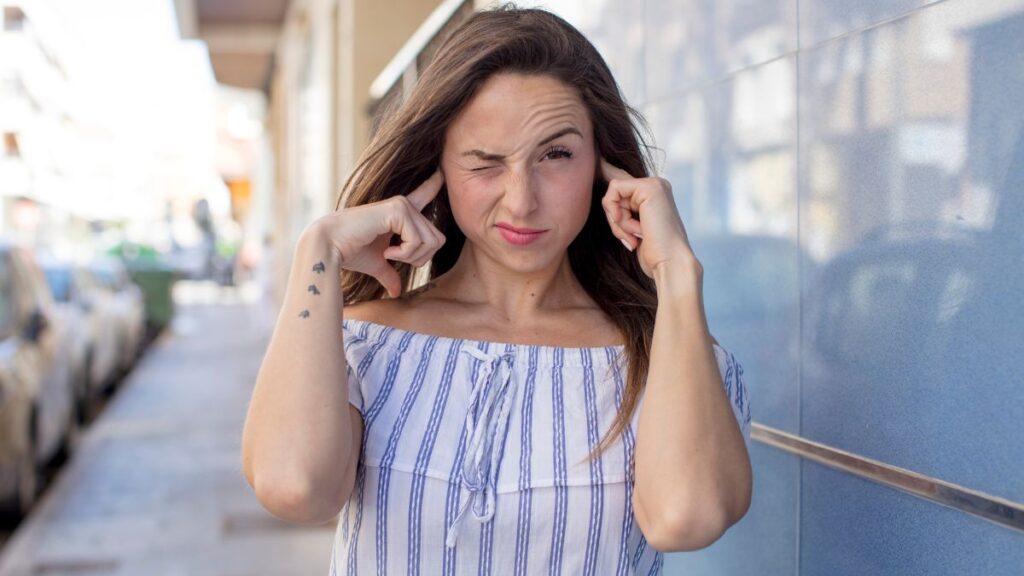 woman holding her ears looking annoyed on a sidewalk