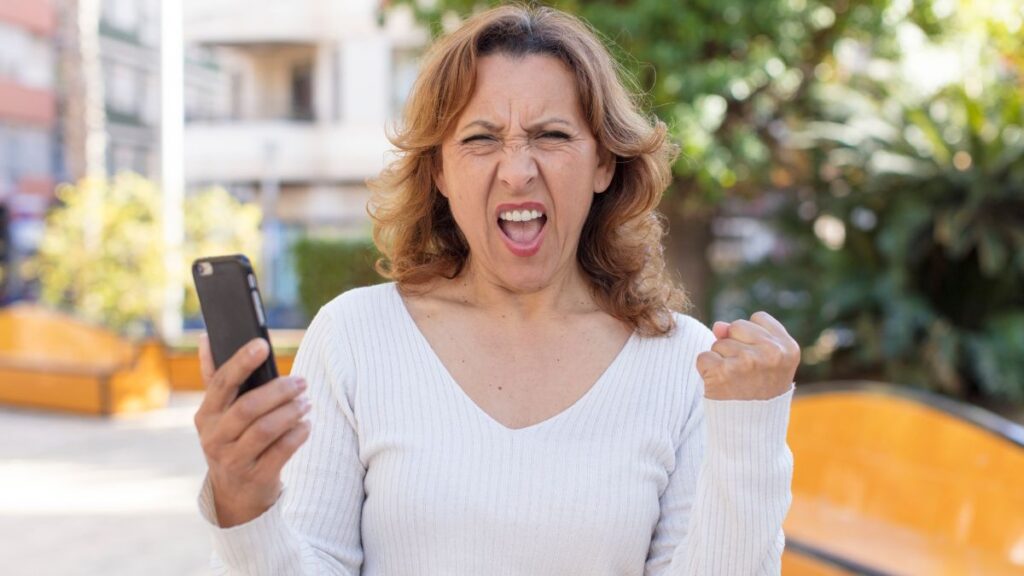 woman holding her fist up mad holding a phone