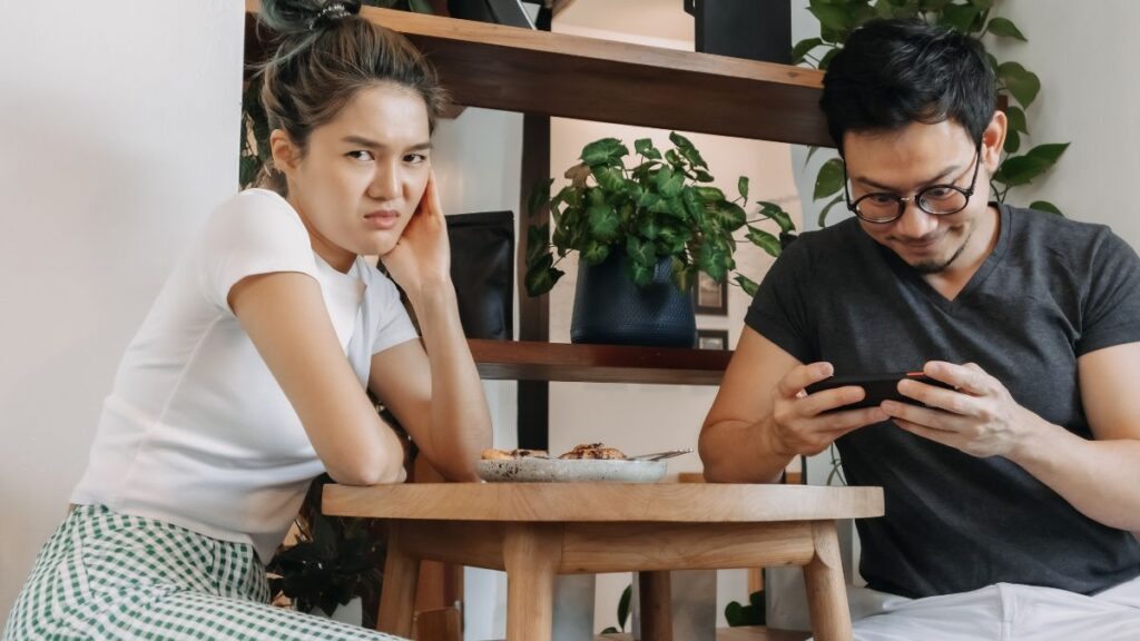 woman looking annoyed at a table with a man on his phone