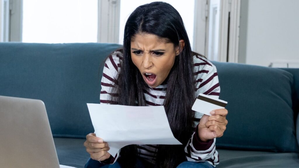 woman looking at her bills shocked, holding a credit card