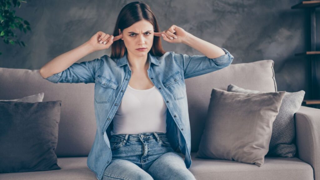 woman looking grumpy on the couch plugging her ears