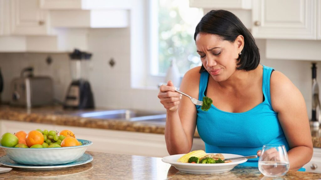 woman looking unhappy eating a plate of food