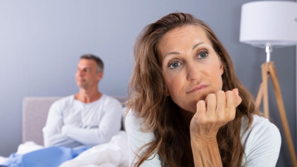 woman looking unhappy while husband sits up in bed also unhappy