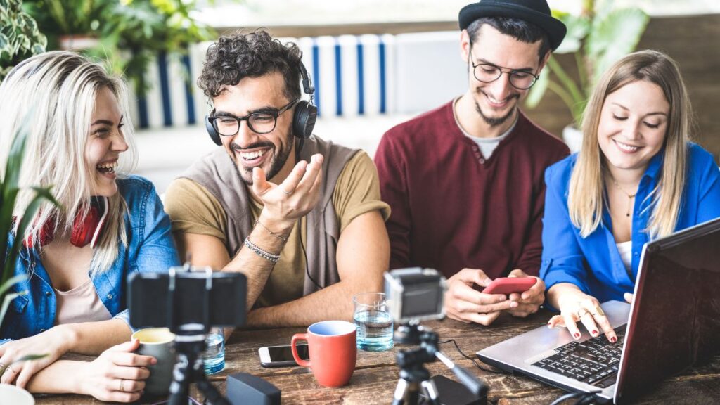 A group of people working on a lap top and soicals with a phone