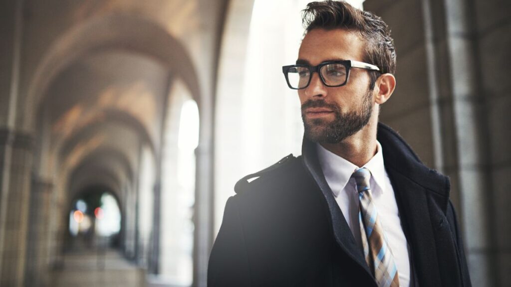 Man well dressed with glasses and a coat on in an old hallway