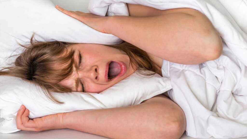 Woman in bed holding a pillow and yawning, can't sleep