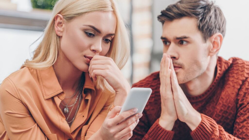 man looking sorry as a woman checks her phone