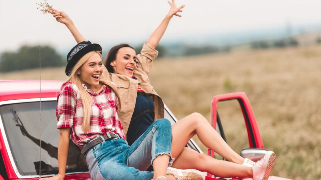 two women sitting on a car smiling