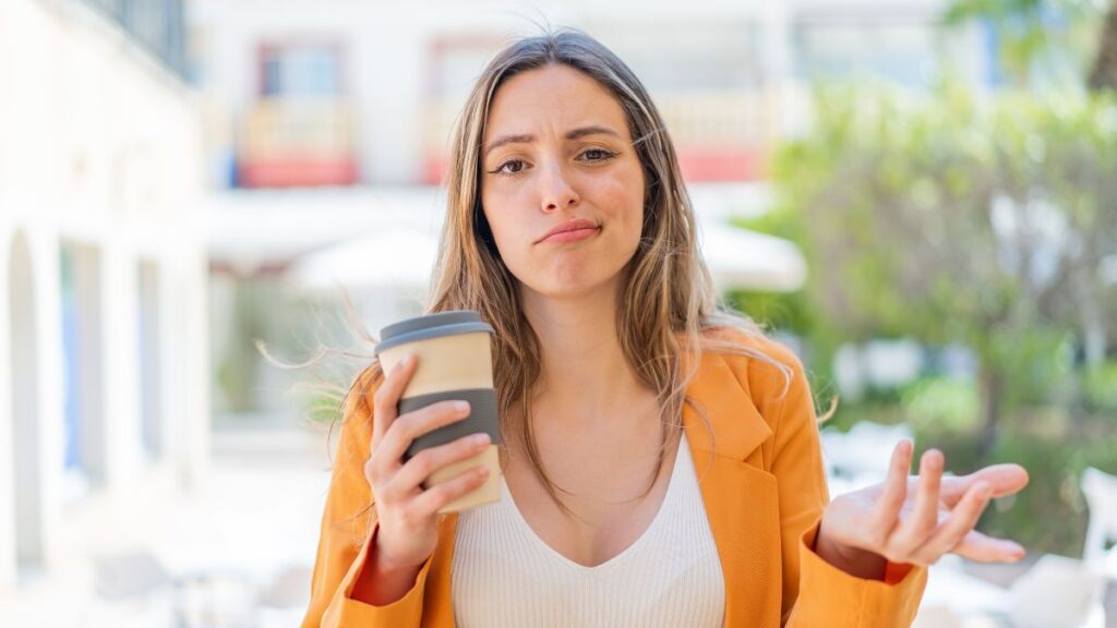 woman holding a coffee shrugging