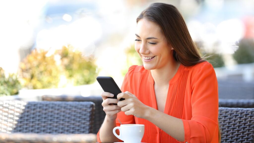 woman sitting with coffee smiling and looking at phone