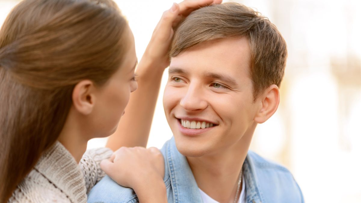 woman with hand on mans head while he smiles