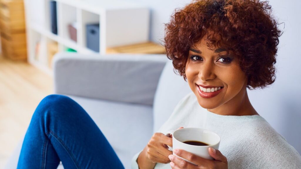 happy woman with coffee sitting on couch smiling