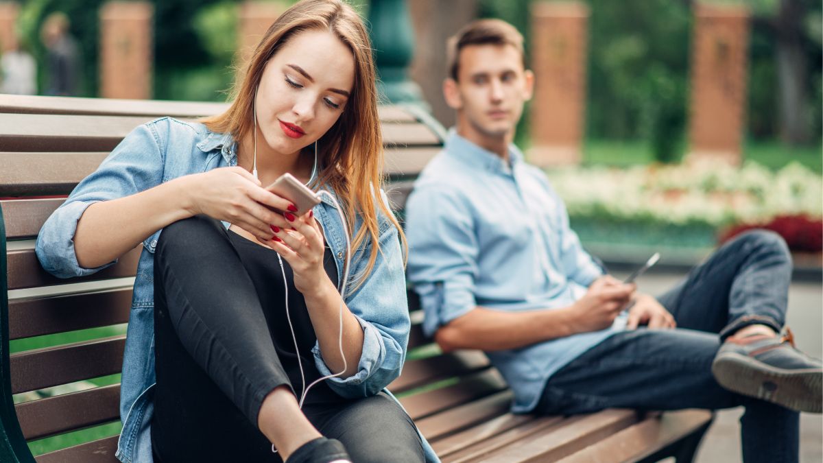 woman looking at phone on bench, man looking at woman