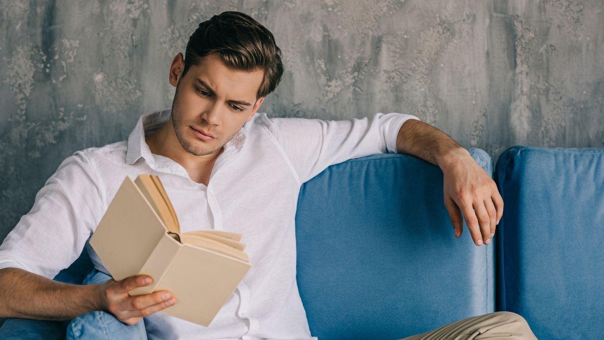 man sitting on a blue couch reading a book