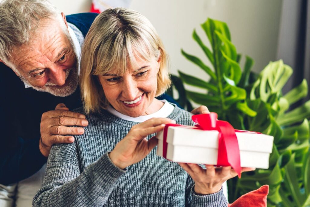 older man behind a women about to open a gift box. 